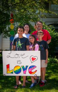 Two adults and two kids hold a sign that says "love is love"