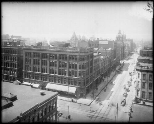 View of intersection of Arapahoe and 17th Streets, in Denver, Colorado; shows Bank Block, towers of Tabor Opera House, Post Office and Mining Exchange buildings, pedestrians and buggies.