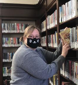 An attractive librarian wearing a face mask shelves a book in the Park Hill Branch Library