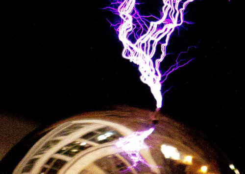 A purple light sparks from the gold surface of a Van de Graff generator