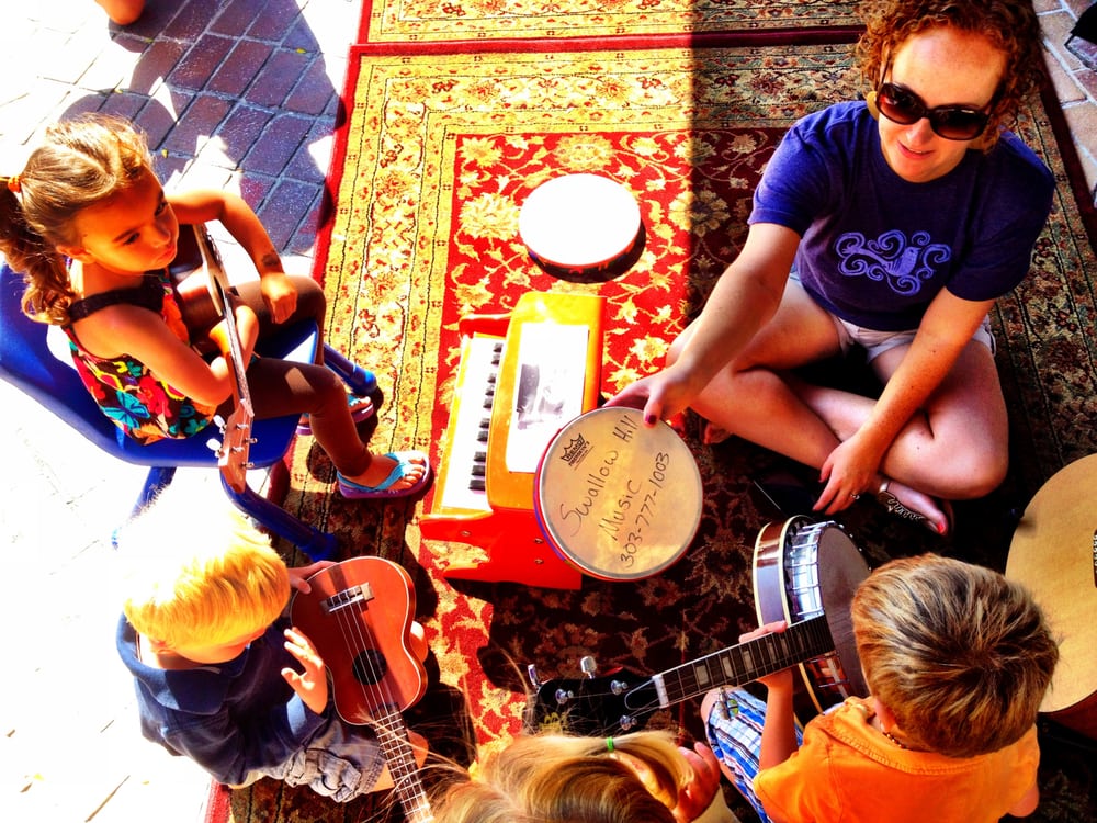 Children sit in a circle with one adult holding a variety of musical instruments