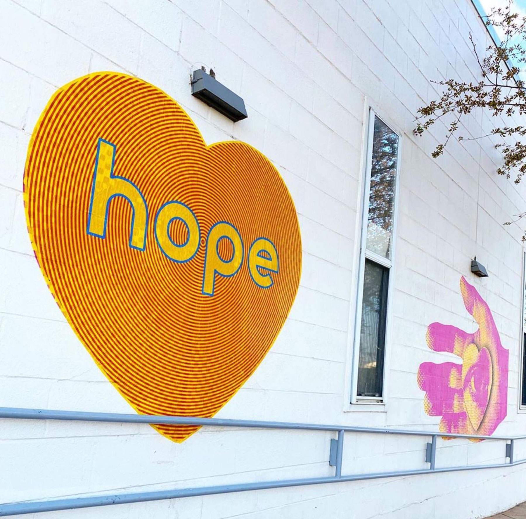 Wheat paste art by Koko Bayer. Orange heart with the word hope in yellow inside the heart pasted on the side of a white building.