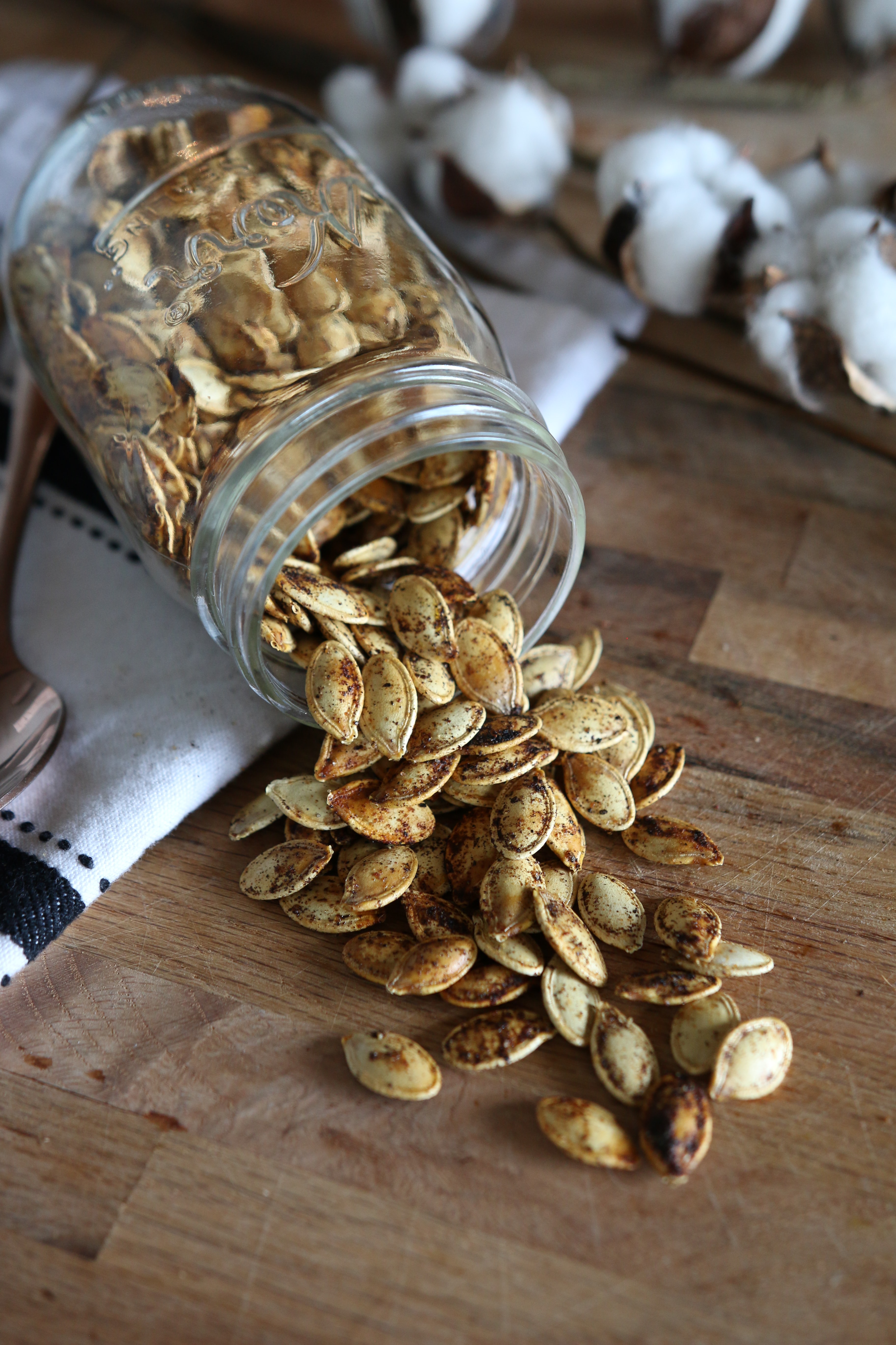 Photograph of a jar tipped over onto a table, spilling out pumpkin seeds