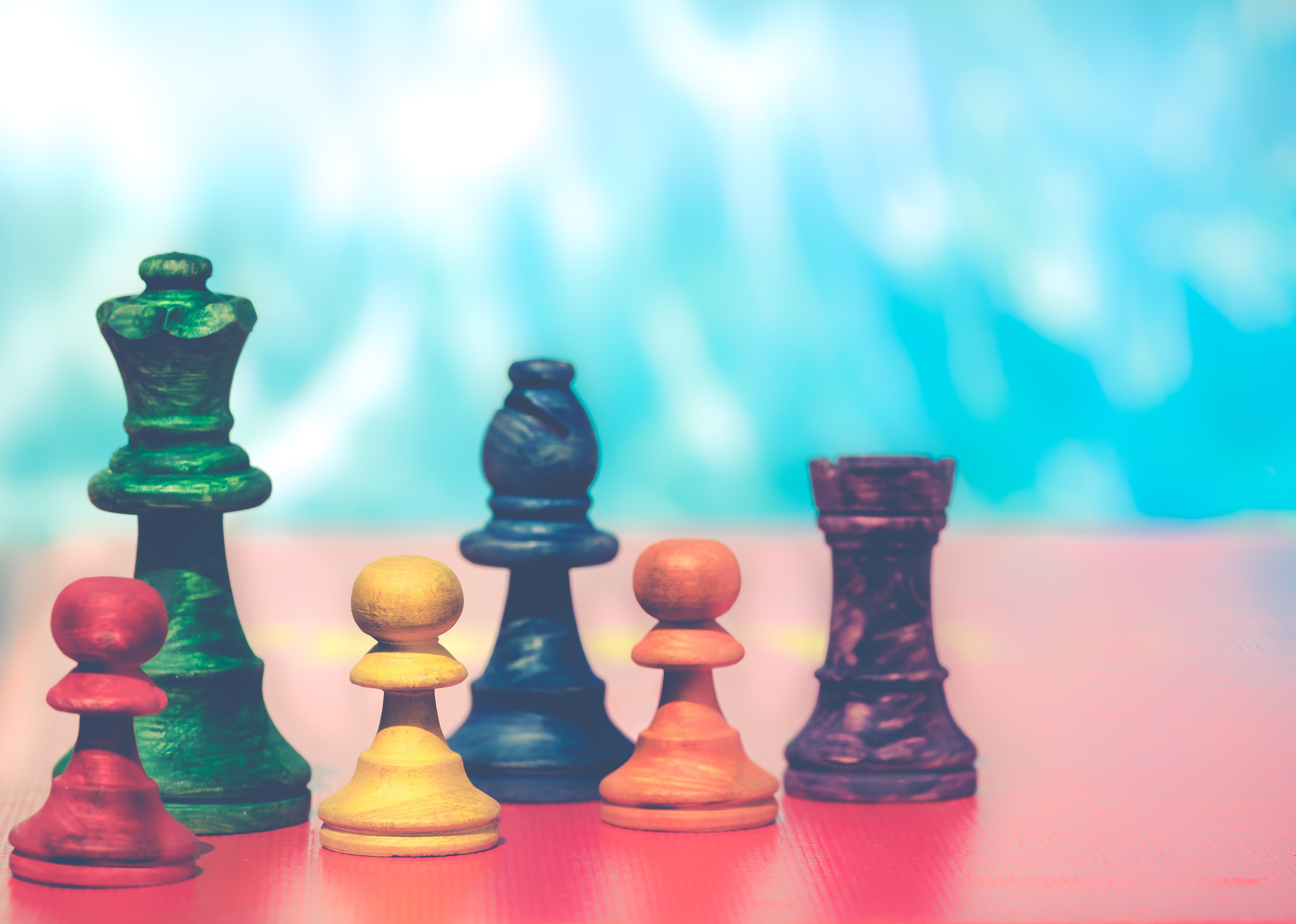 a set of 5 rainbow colored chess pieces sit in a row on a table. 