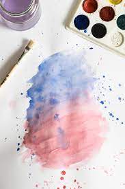 paints and paintbrush next to pink and blue watercolor painting 