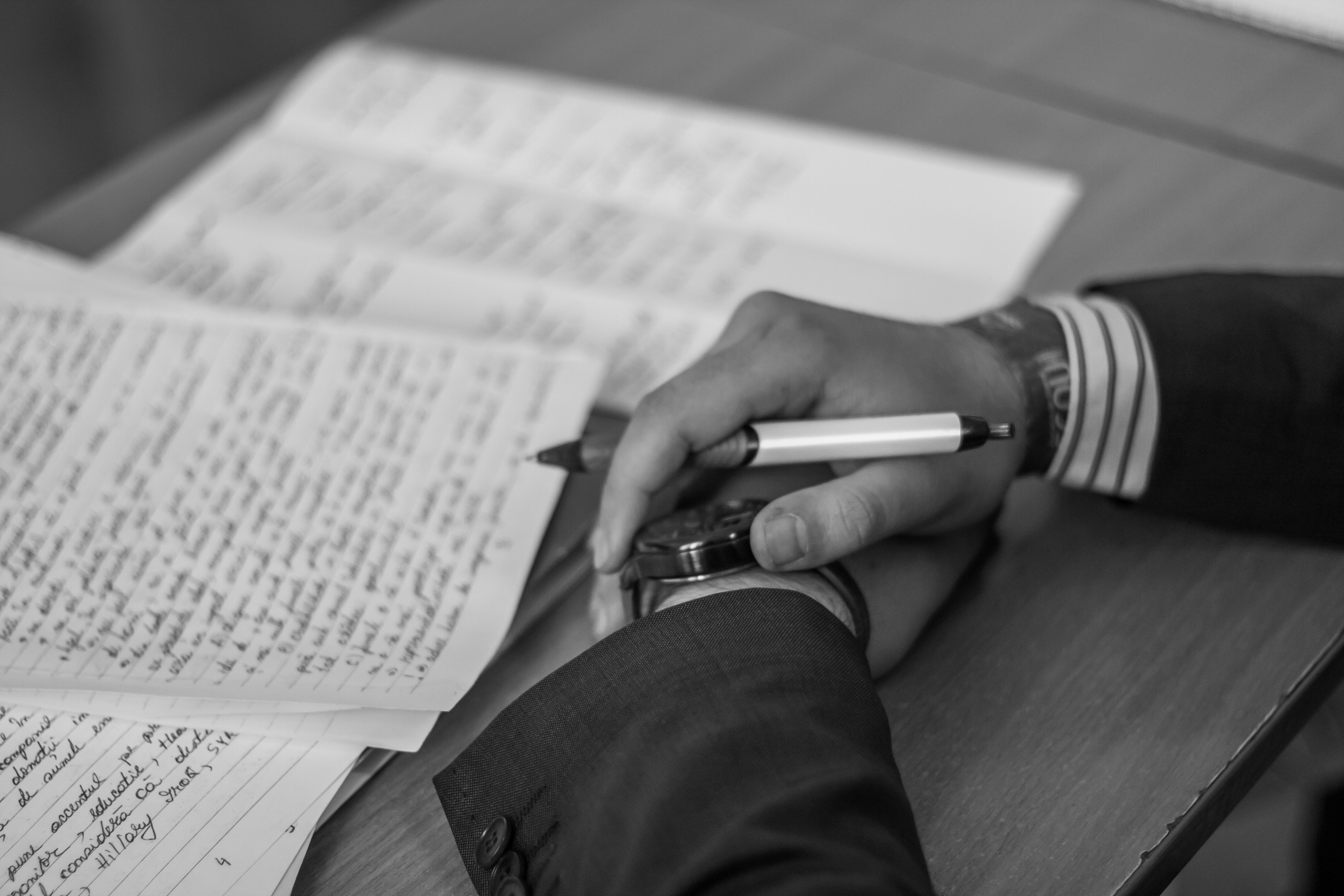 Black and photo of hands holding a pen over a page of hand written notes.