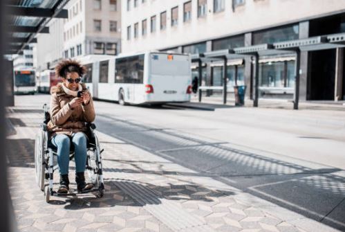 Smiling woman in a wheelchair sits on an urban plaza next to a bus
