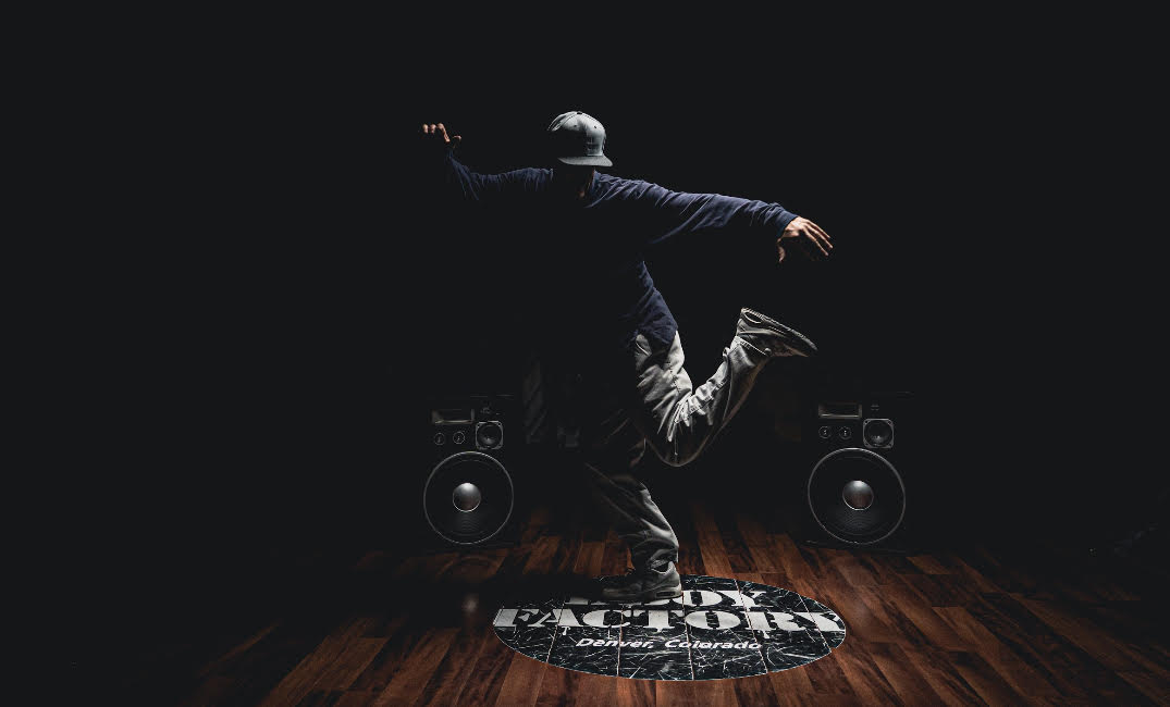 Dancer Between two large speakers with floor sticker that reads bboy