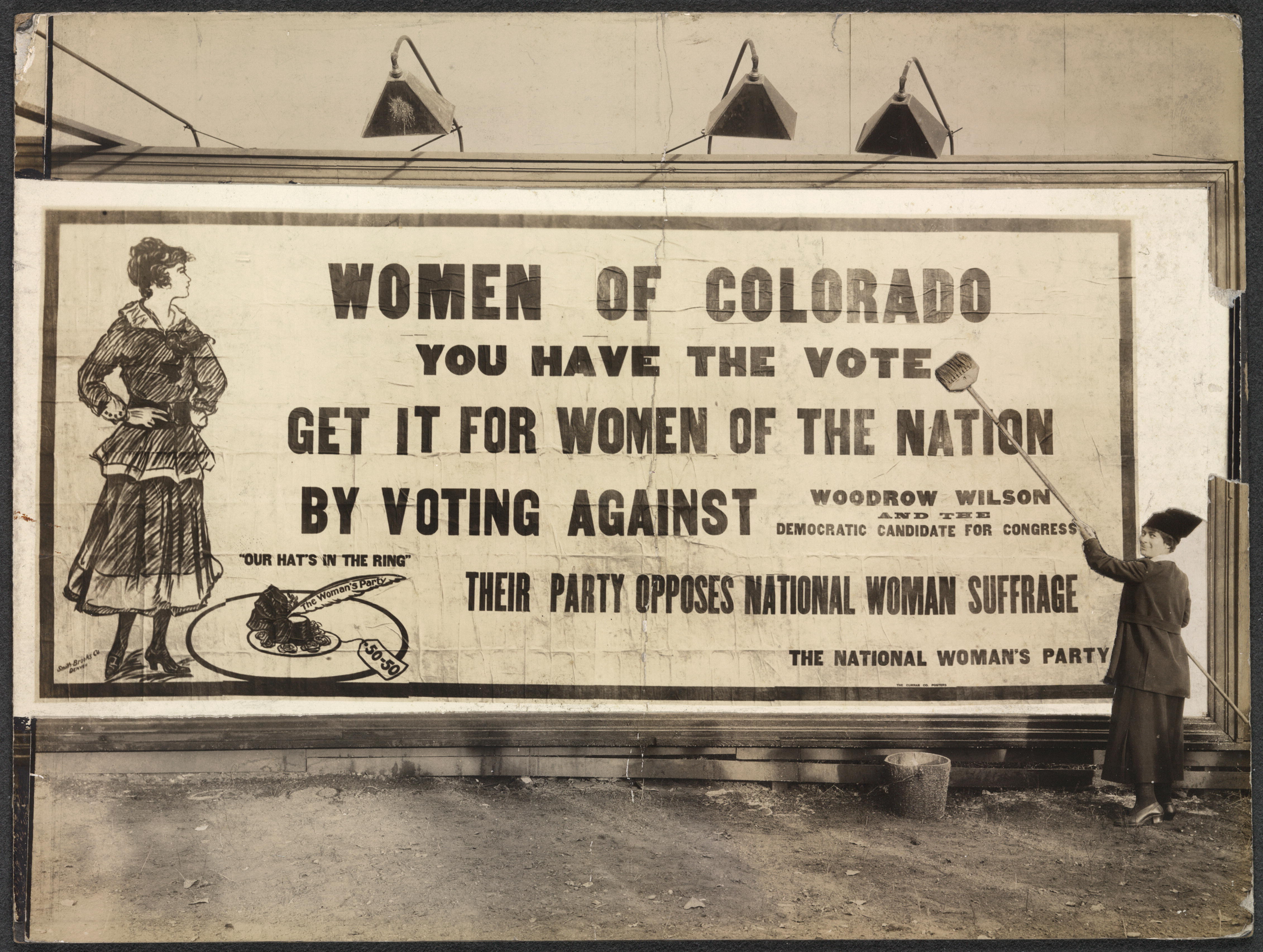 Photograph of unidentified woman putting up billboard with bucket and broom. Billboard reads: "'Women of Colorado, you have the vote. Get it for women of the nation by voting against Woodrow Wilson and the Democratic Candidate for Congress. Their party opposes national woman suffrage. The National Woman's Party." Billboard features image of young woman and a hat with "The Woman's Party" feather and a "50-50" price tag, above which is the motto "Our Hat's in the Ring."