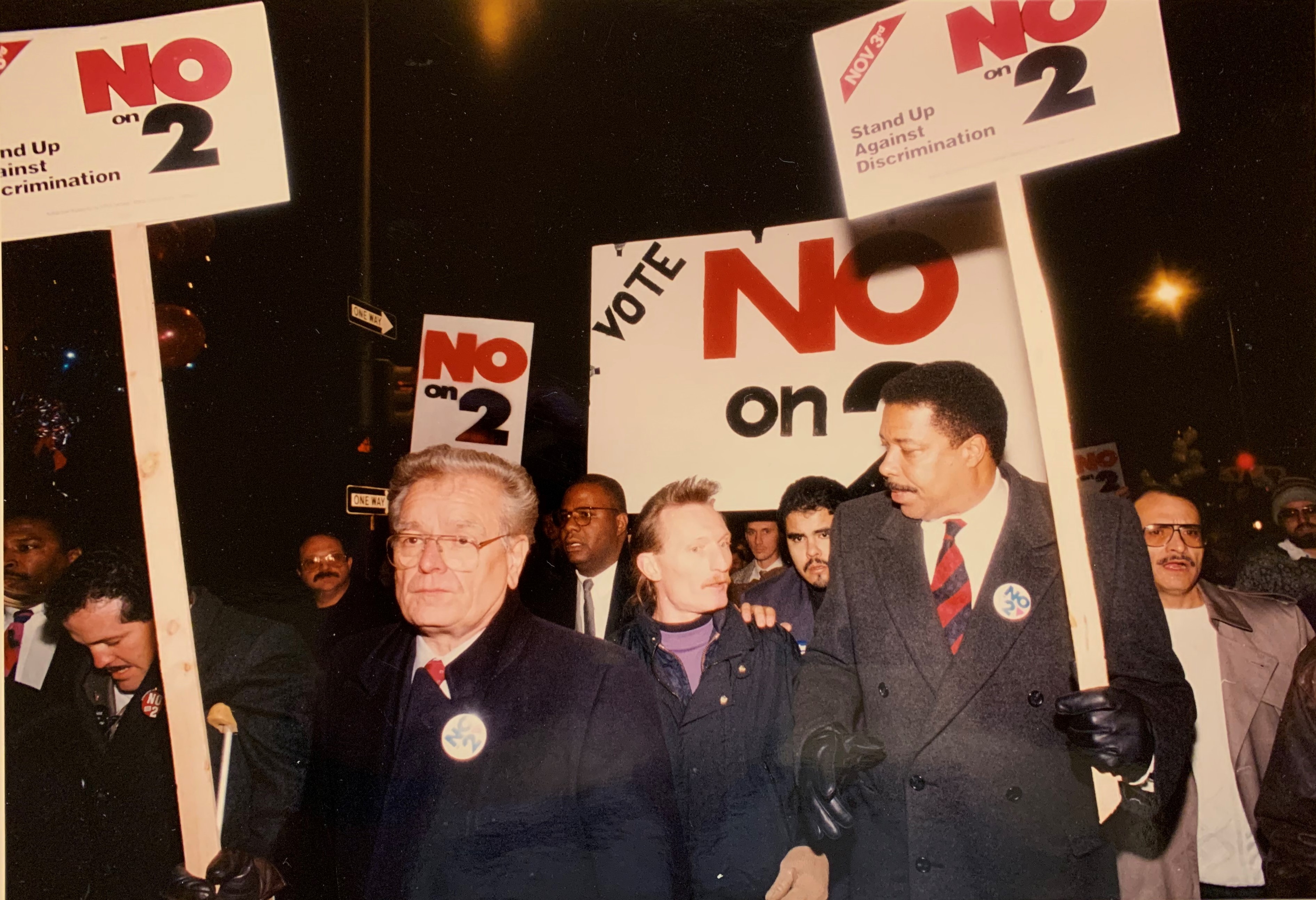 Photo of protesters with signs saying "vote no on 2". Includes Mayer Webb among protesters. 