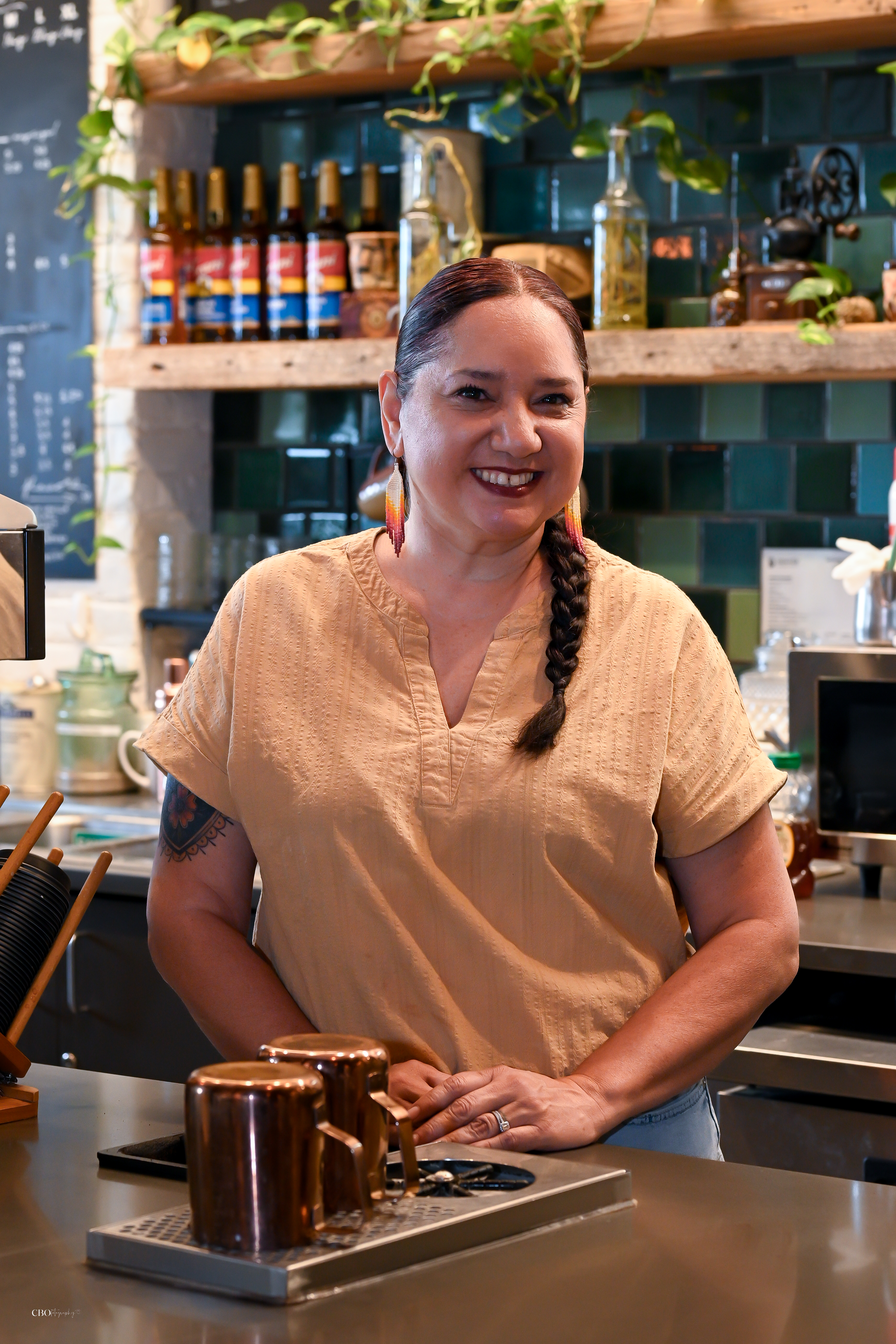 Charleen smiling in an orange shirt behind the counter at her cafe.