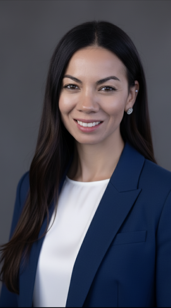 Esmeralda smiling in a blue blazer and a gray back drop.