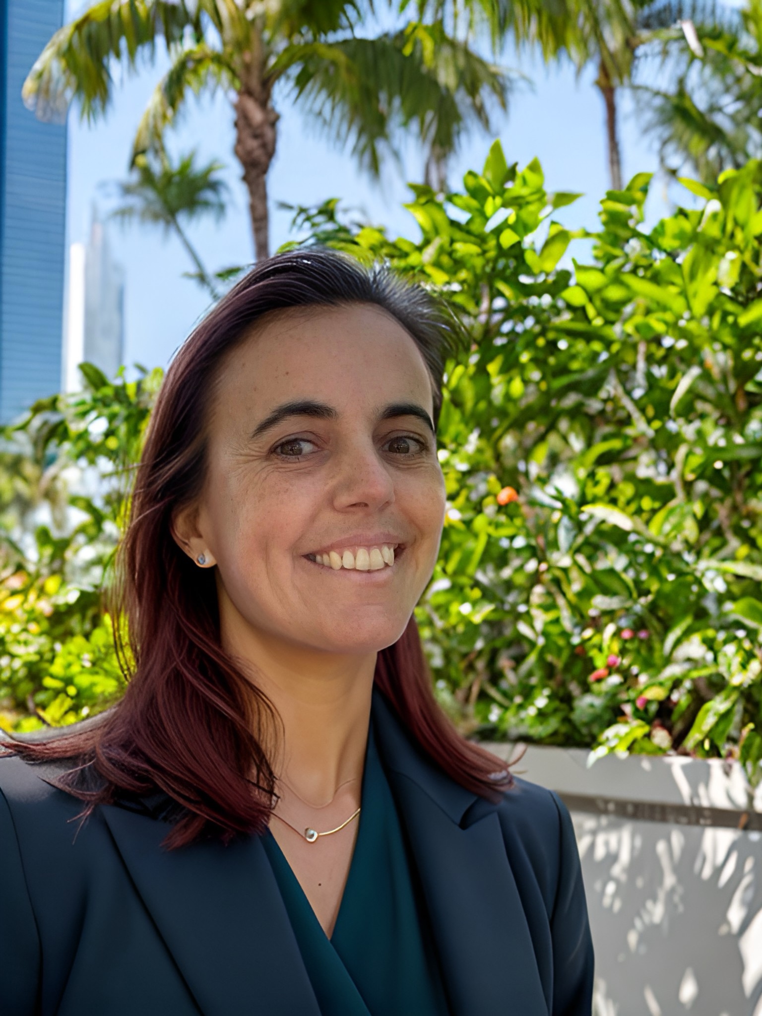 Julia smiling in a black blazer with palm trees behind her.