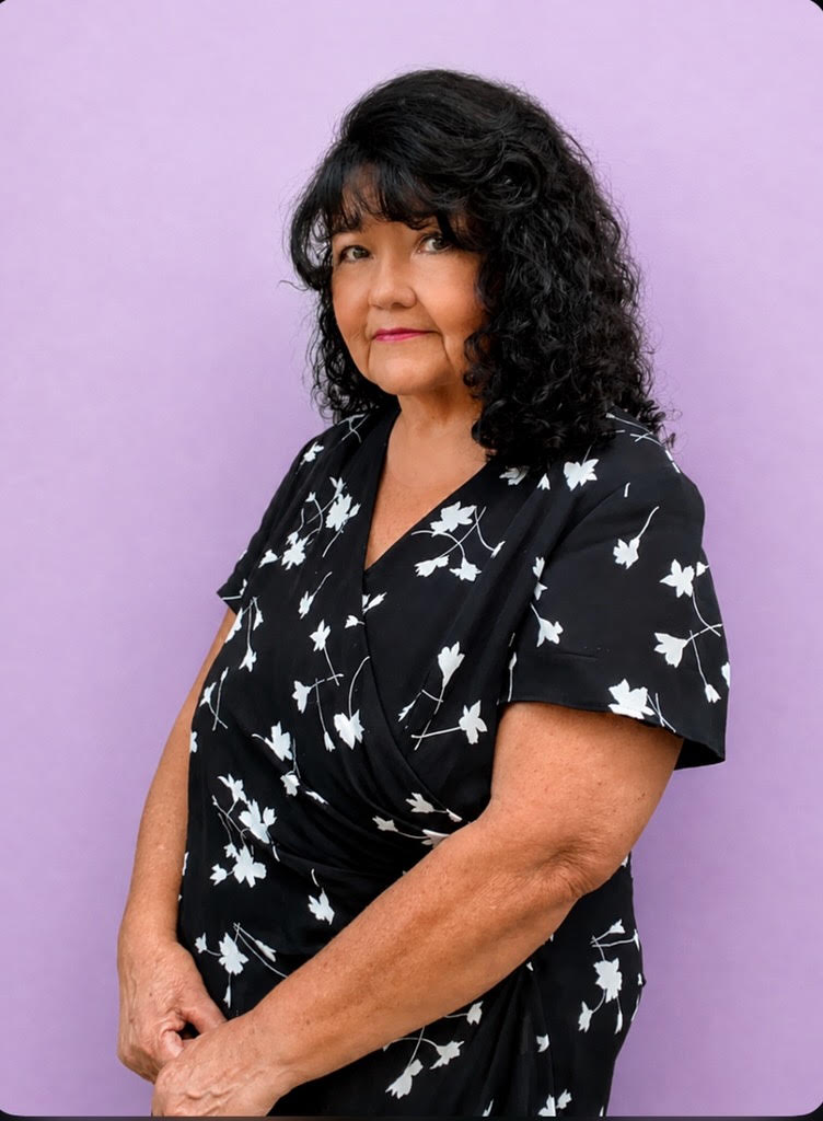 Sandra smiling in a black and white floral patterned shirt and a purple back drop.