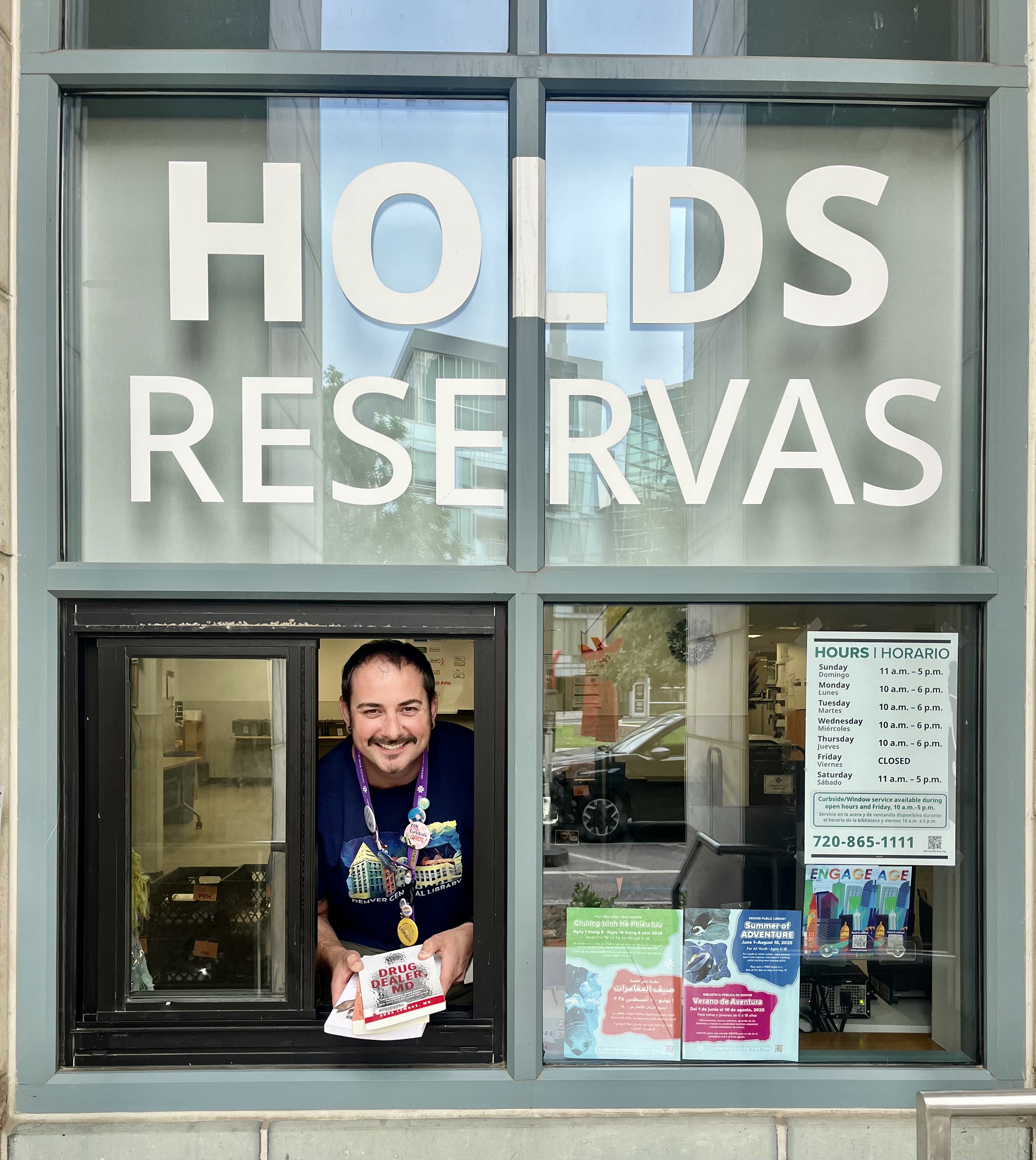 Male staff holding books at Central's curbside holds pickup window