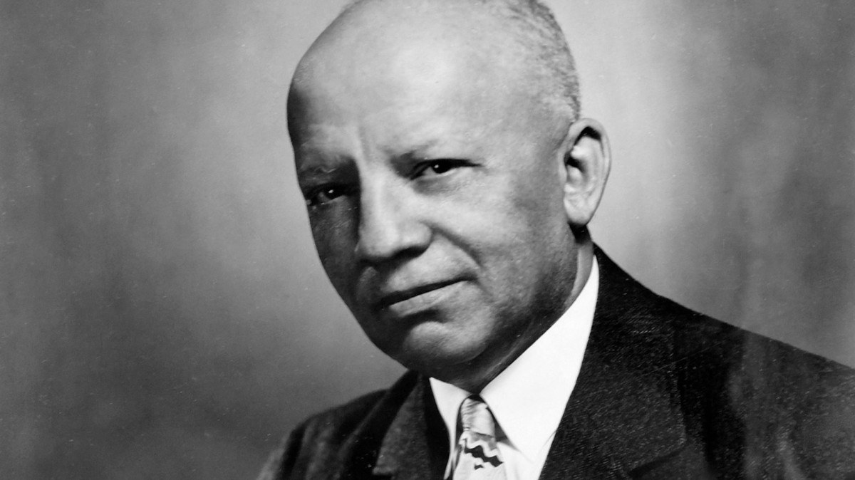 Black and white portrait of Carter G Woodson with a soft background. He is wearing a black suit.