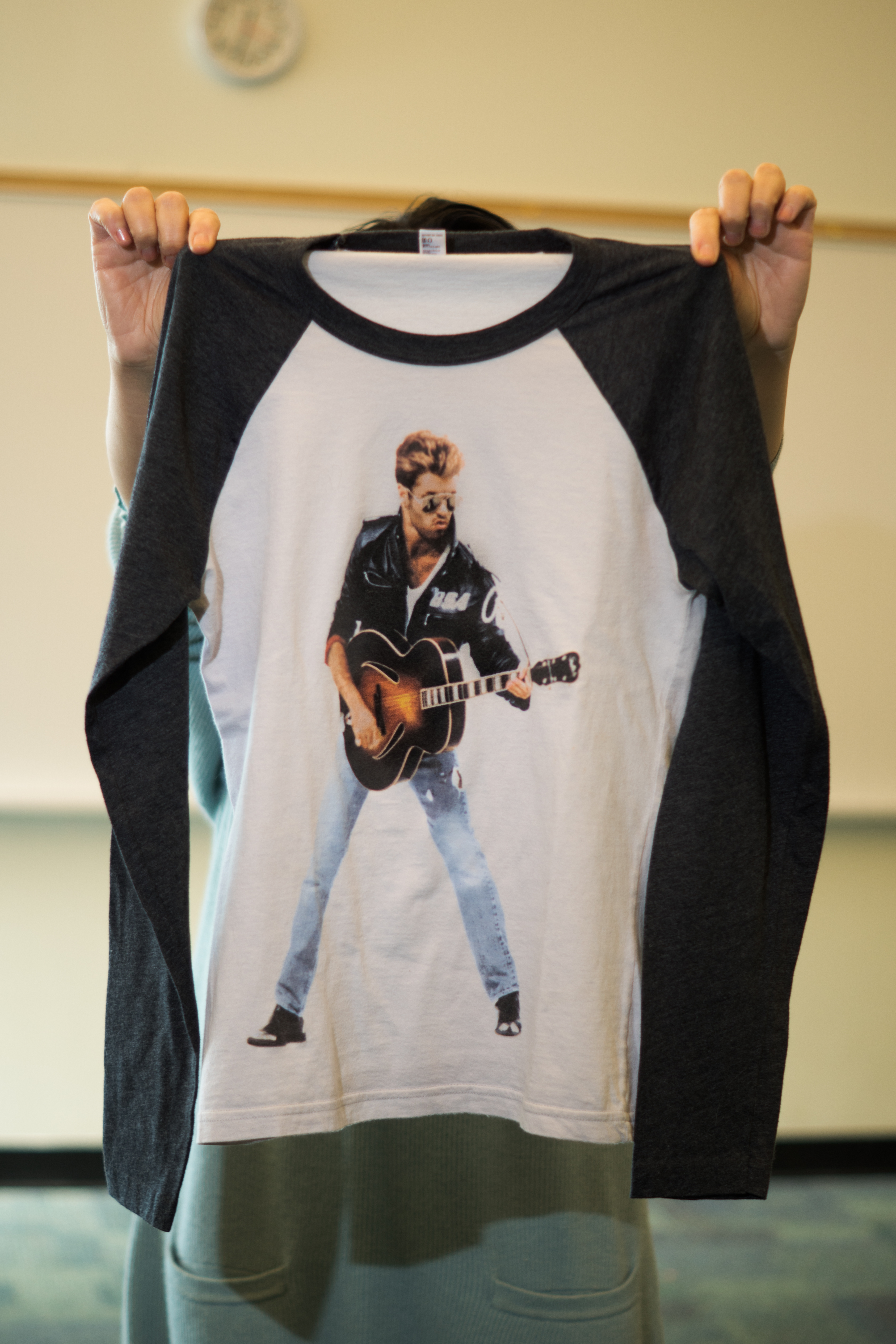 Woman holding a t-shirt with a picture of George Michael playing guitar
