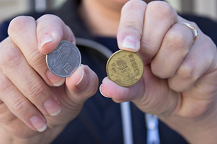 Photograph of a woman holding a silver coin in one hand and a gold coin in the other