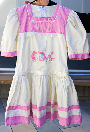 Photograph of a hand holding a child's pink and white dress