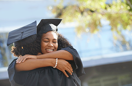 Two people in graduation caps and gowns hugging
