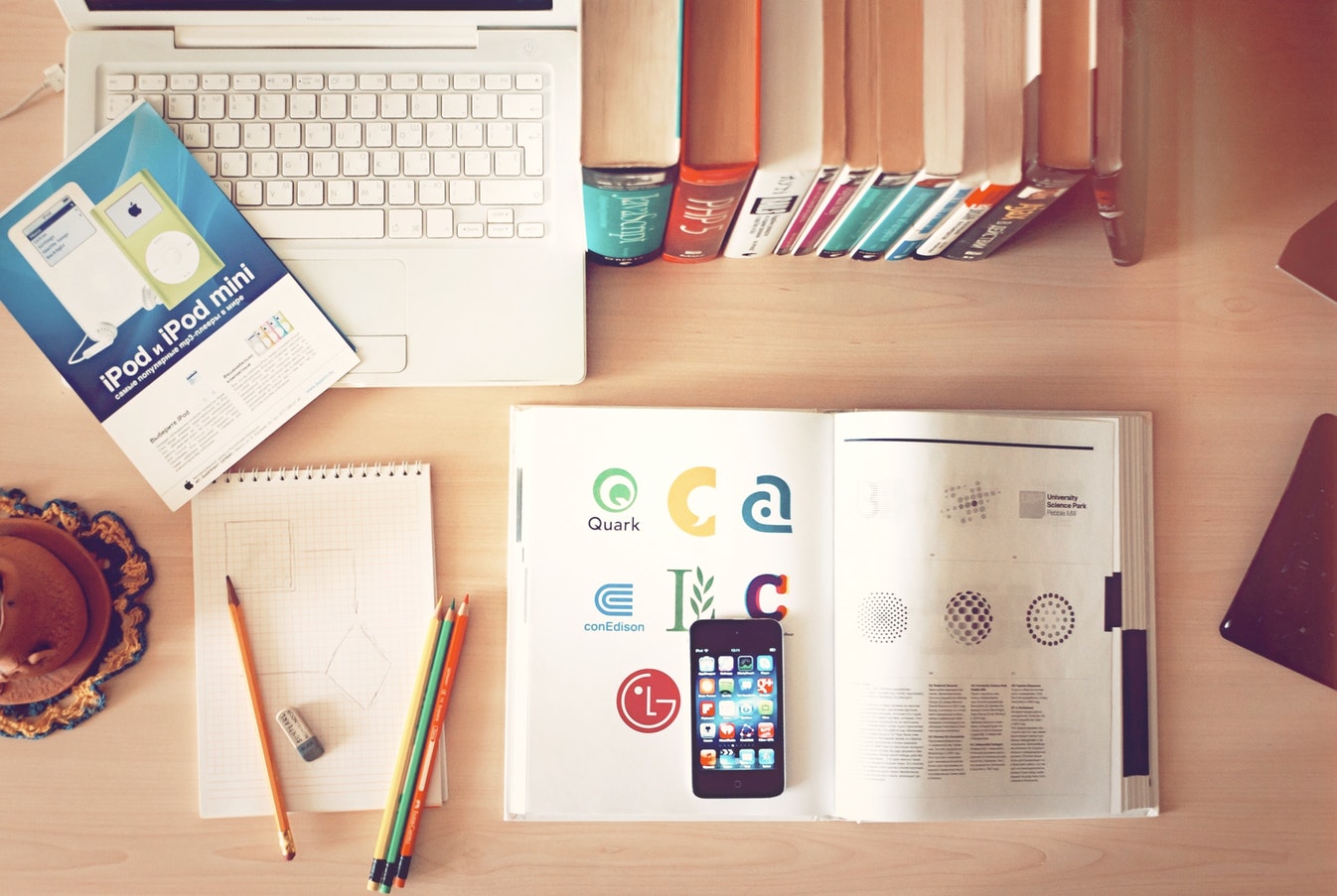Desk with books, sketch paper, pencils, and a logo design book