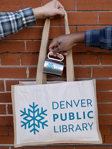Image of people holding library-branded tote bag and carabiner mug