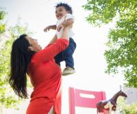 Woman holding smiling young child up in the air.