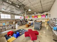 Interior photograph of library, high ceiling, industrial but colorful space with bookshelves and colorful seating. 