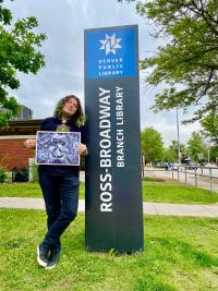 Mar Williams stands outside of the Ross-Broadway branch holding a piece of their art
