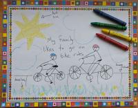 A drawing of two people biking on a sidewalk next to grass and dandelions. There are crayons lying on the paper.