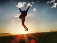 Silhouette of a person jumping with both arms in the air, with sunset behind