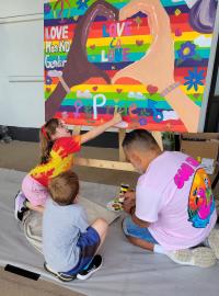 An adult and two young children working on a Pride mural 