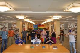 Denver Public Library staff wearing facial coverings and posing with their hands forming heart shapes around a Pride (rainbow) flag