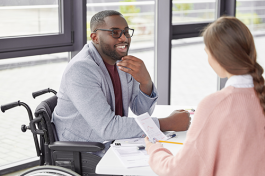 Man in wheelchair smiling across workspace at female coworker