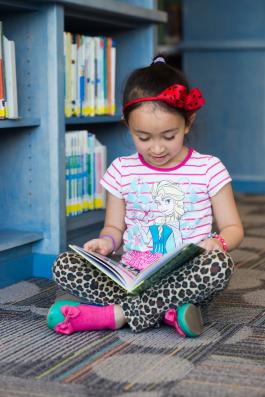 Child sitting on floor of library, reading book