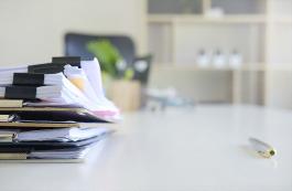 Stack of files sitting on a desk with a pen laying nearby.