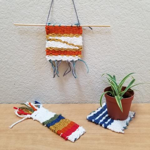 Photo of three weavings made on DIY looms. One hung from a rod for display, one square-shaped weaving used as a coaster for a plant, and a third woven at bookmark size.