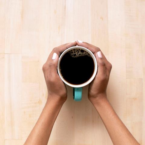 hands touching coffee cup on wood surface