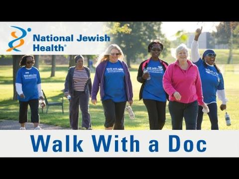 This photo shows a group of people walking in the park, including the Blue and Gold National Jewish Logo and the Walk With a Doc branding. 