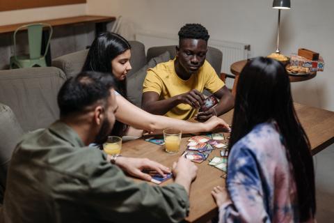 a group of four teens gather around a table playing a card game. 