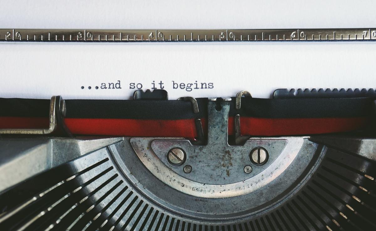 Close-up photo of a typewriter with the phrase "...and so it begins" on the paper