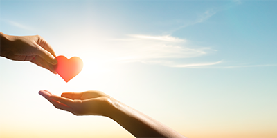 A hand gives a red heart to another.