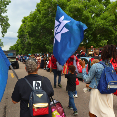 Parade-goers at the Juneteenth parade represent the Denver Public Library with DPL branded flags and banners.